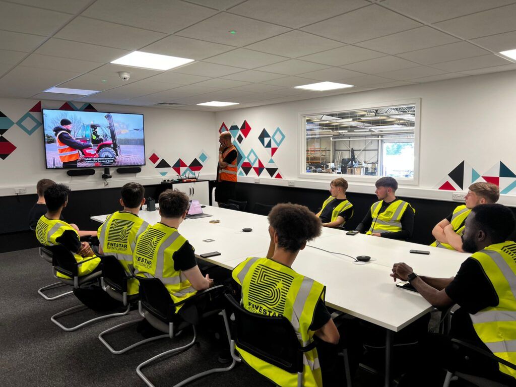 Crew sat in a classroom, wearing hi-viz, watching one of Five Star's training videos.